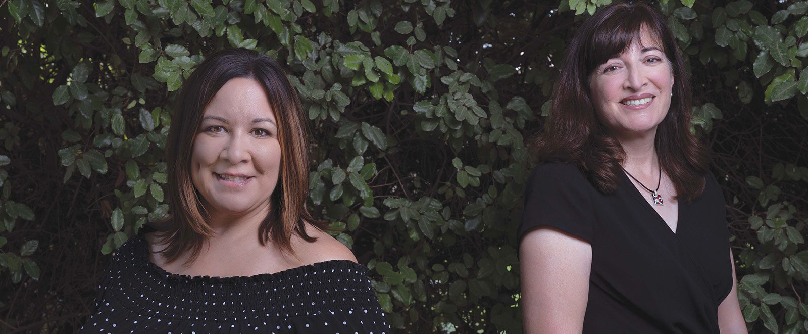 Photo of sisters Christina O’Connell (’96 BSN, ’21 DNP) and Gabriella Blakey (’06 MA, ’13 EDD) standing in front of vines