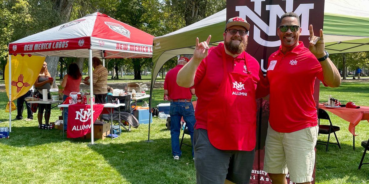 two men in red lobo gear outside of bbq event make the lobo hand sign