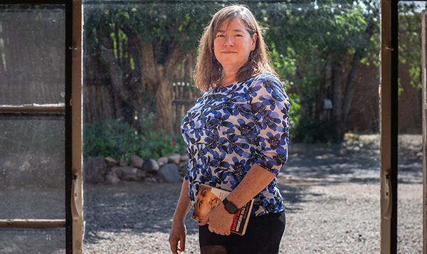 Theresa Duncan wearing a floral print shirt holding a book in her backyard