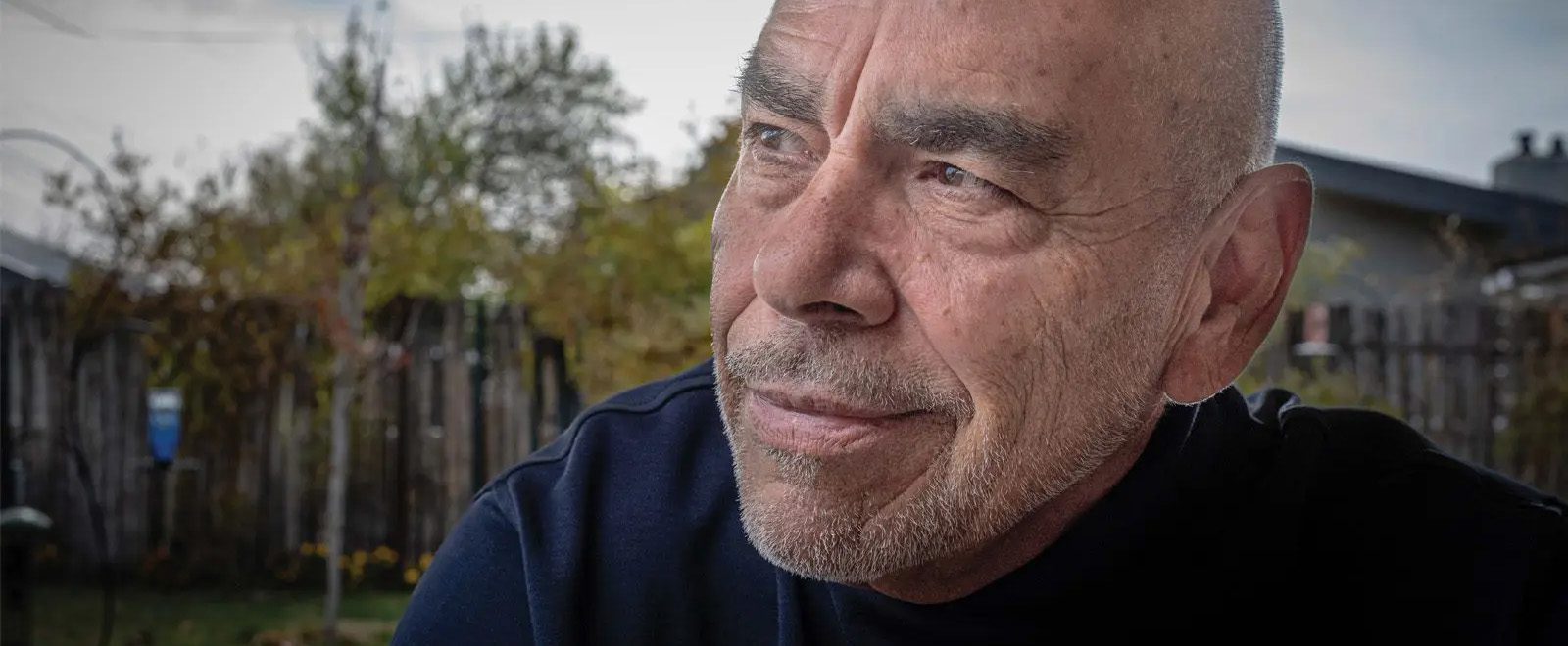 baca-banner poet Jimmy Santiago Baca sits in yard with black shirt on