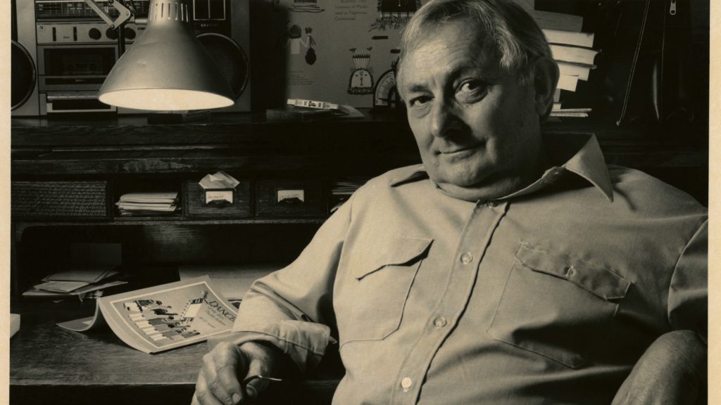 vintage image of Tony Hillerman leaning back at desk in button up shirt