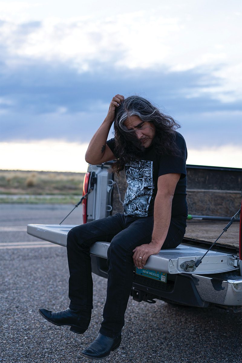 Raven Chacon seated on a truck bed outdoors at dusk