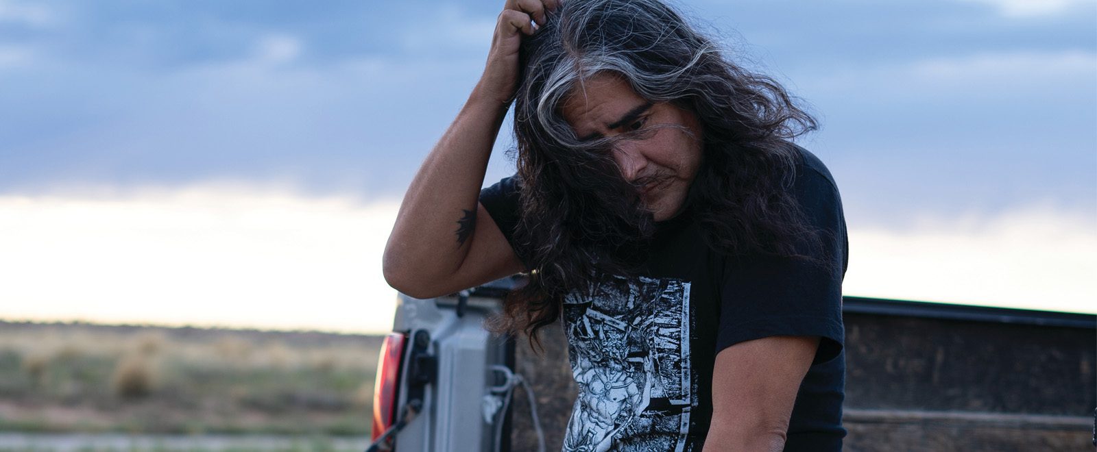 Raven Chacon seated on a truck bed outdoors at dusk