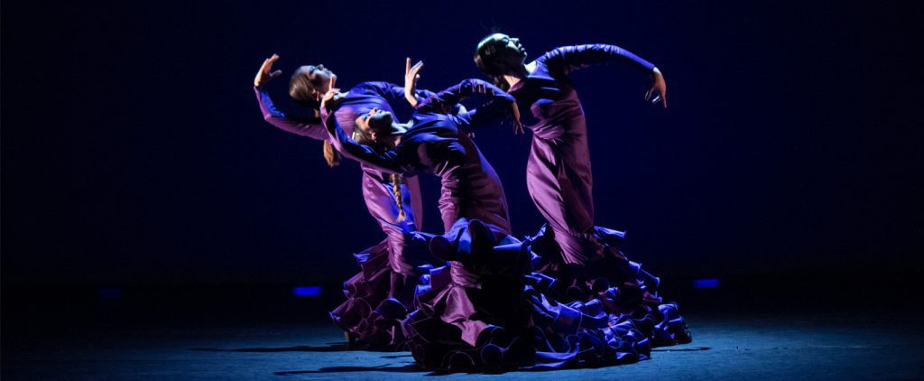 three flamenco dancers in purple dresses perform on stage