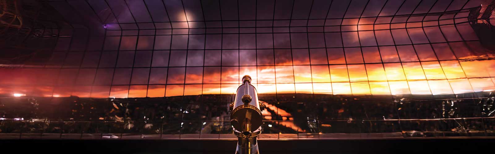 Telescope pointing at a sunset over a city